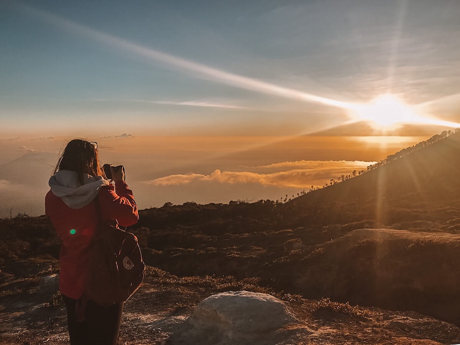 Girl taking picture of sunrise after hiking Ijen volcano