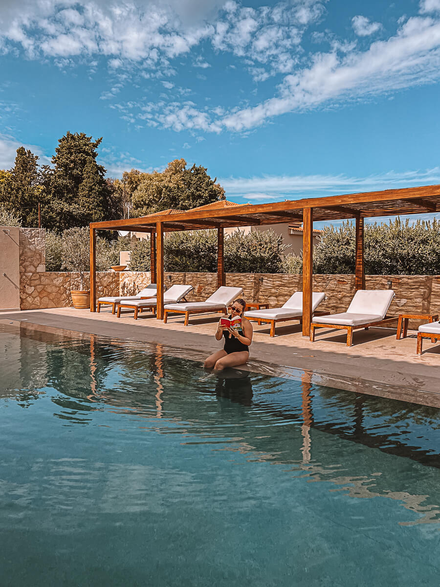 Girl in black swimming costume reading in a large pool on a reading retreat in Greece 